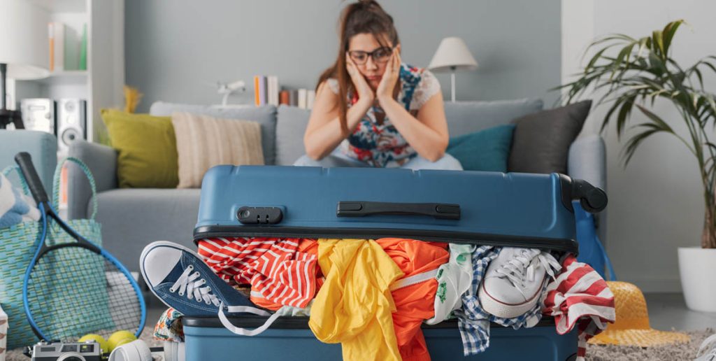a person looking stressed while trying to pack an overfilled suitcase
