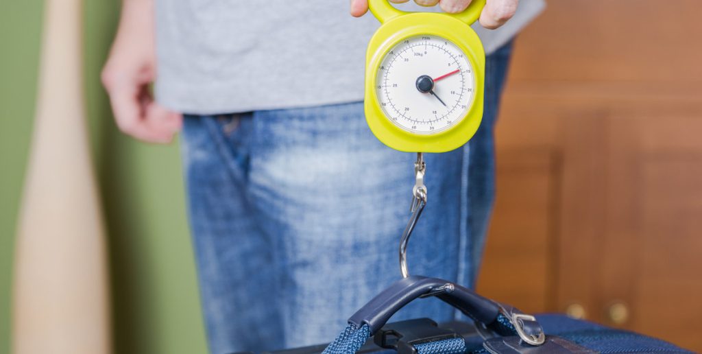 person using a portable luggage scale to weigh a suitcase