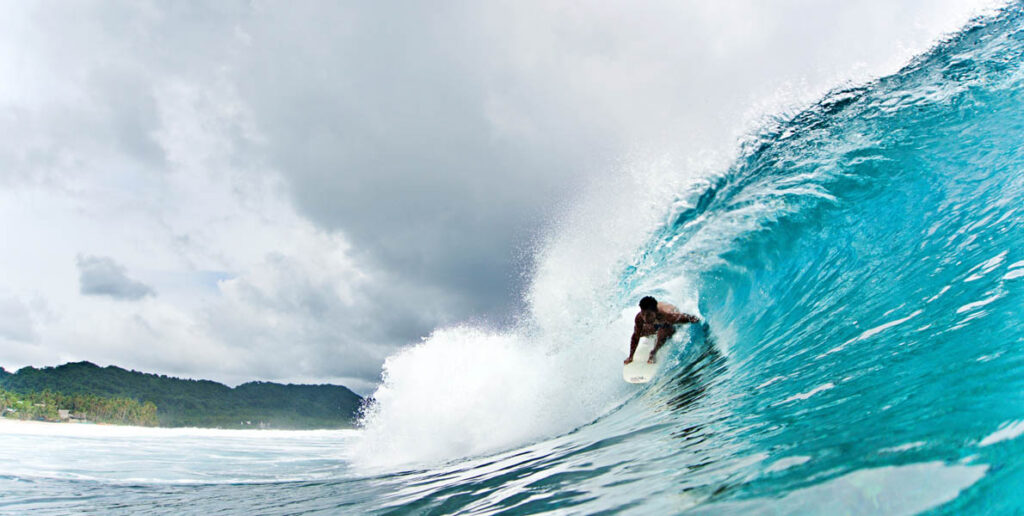 The image appears to show a surfer riding inside a hollow, crystal-clear barrel wave in Siargao.